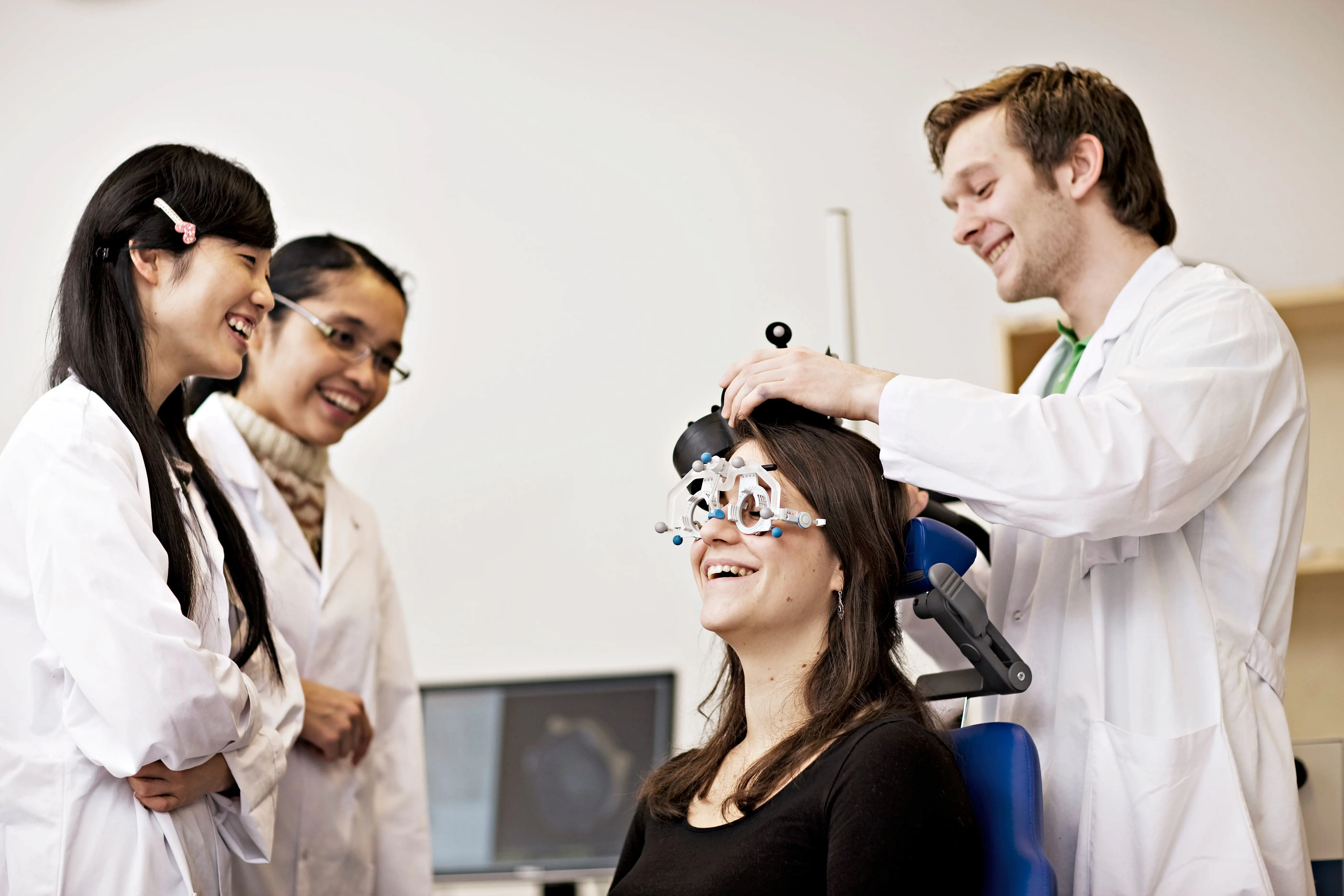 En mannlig lege fester noe på hodet til en kvinnelig pasient. To kvinnelige leger ser på.