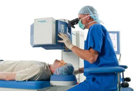 Bilde av en lege som ser inn i et laserapparat. Under ligger en pasient på en benk.