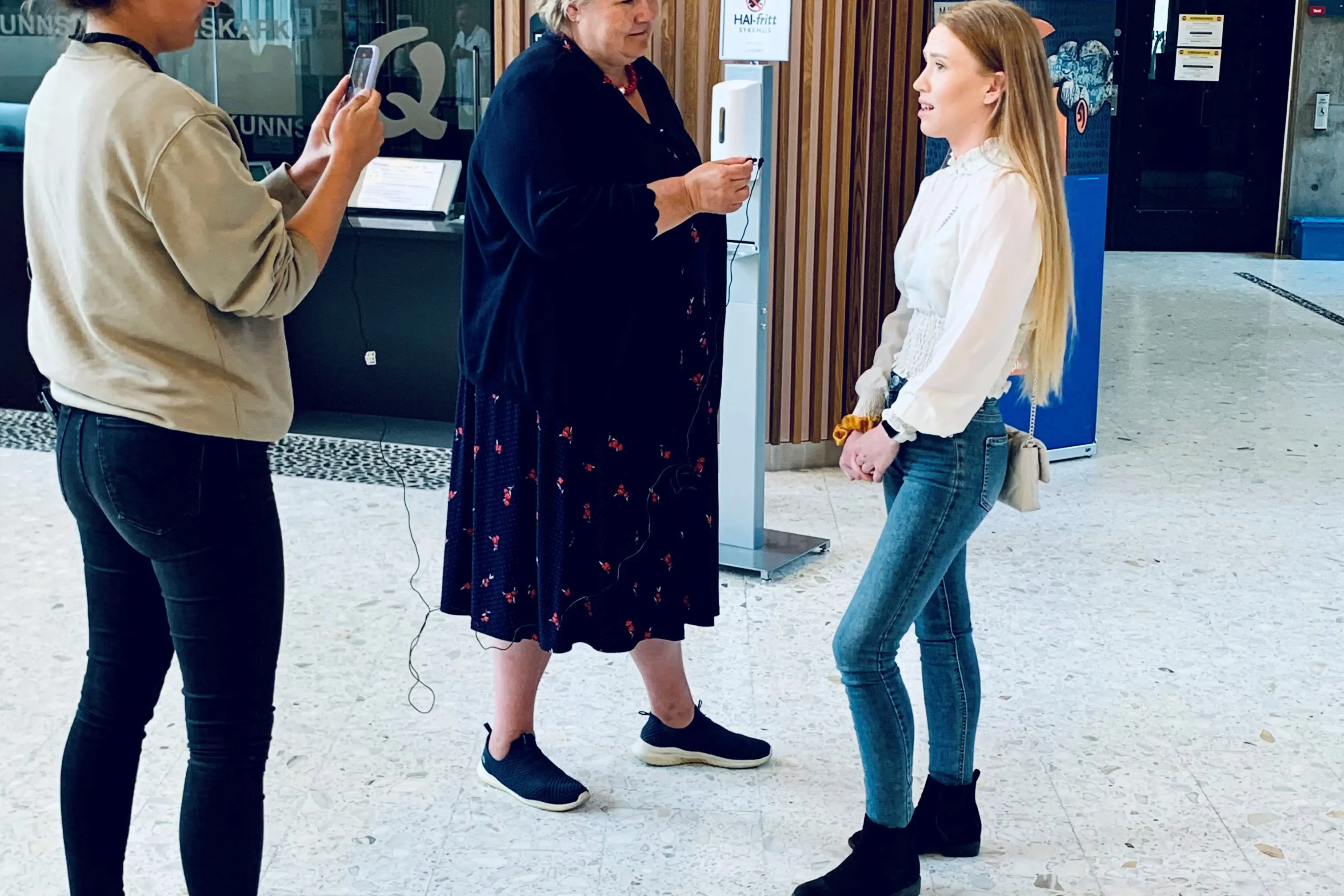 Statsminister Erna Solberg intervjuer en dame. En annen dame står ved siden av og tar bilde.