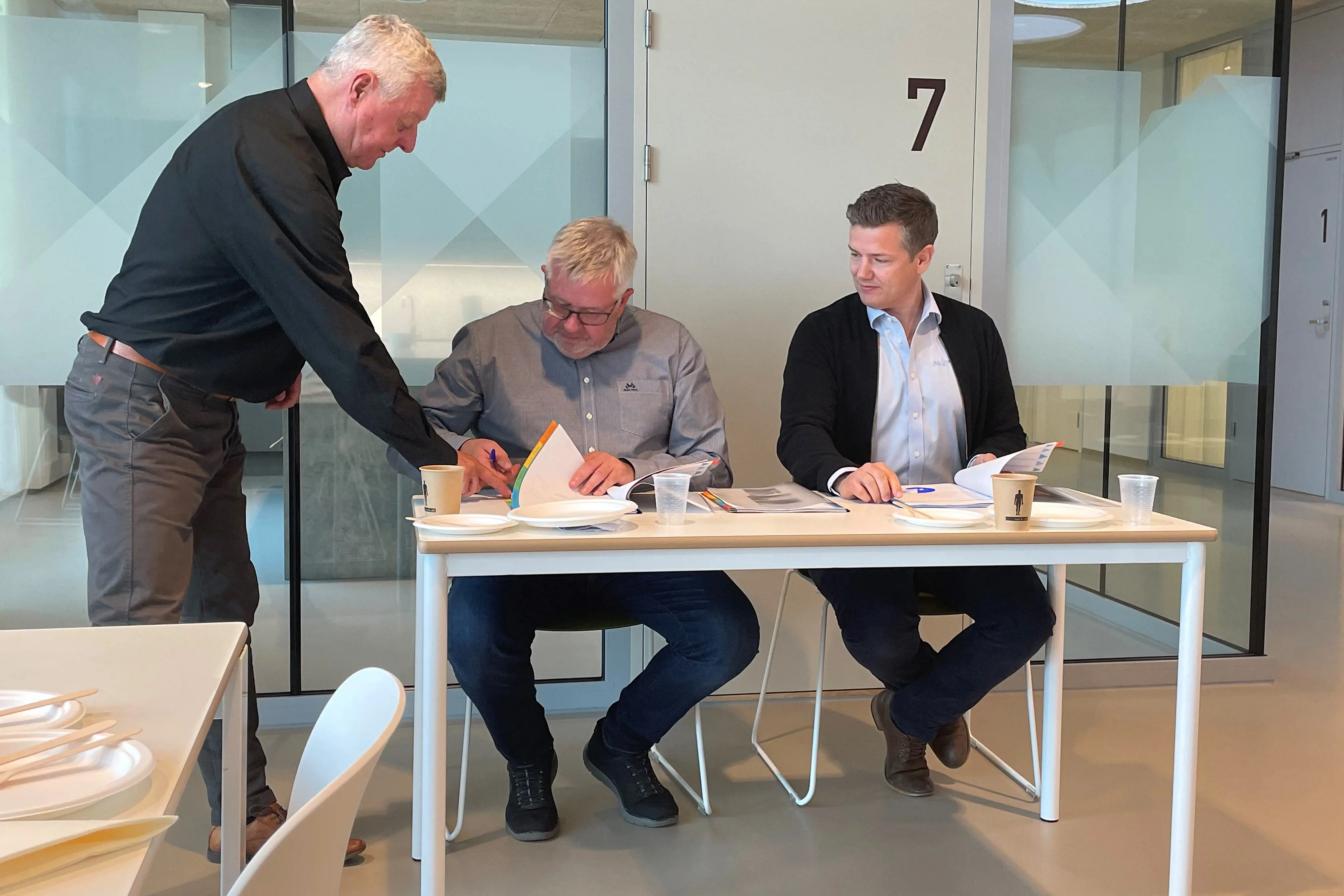 Bjørn Remen står ved bordet til venstre, Jan Morten Søraker signerer, Lars Petter Gamlem til høyre