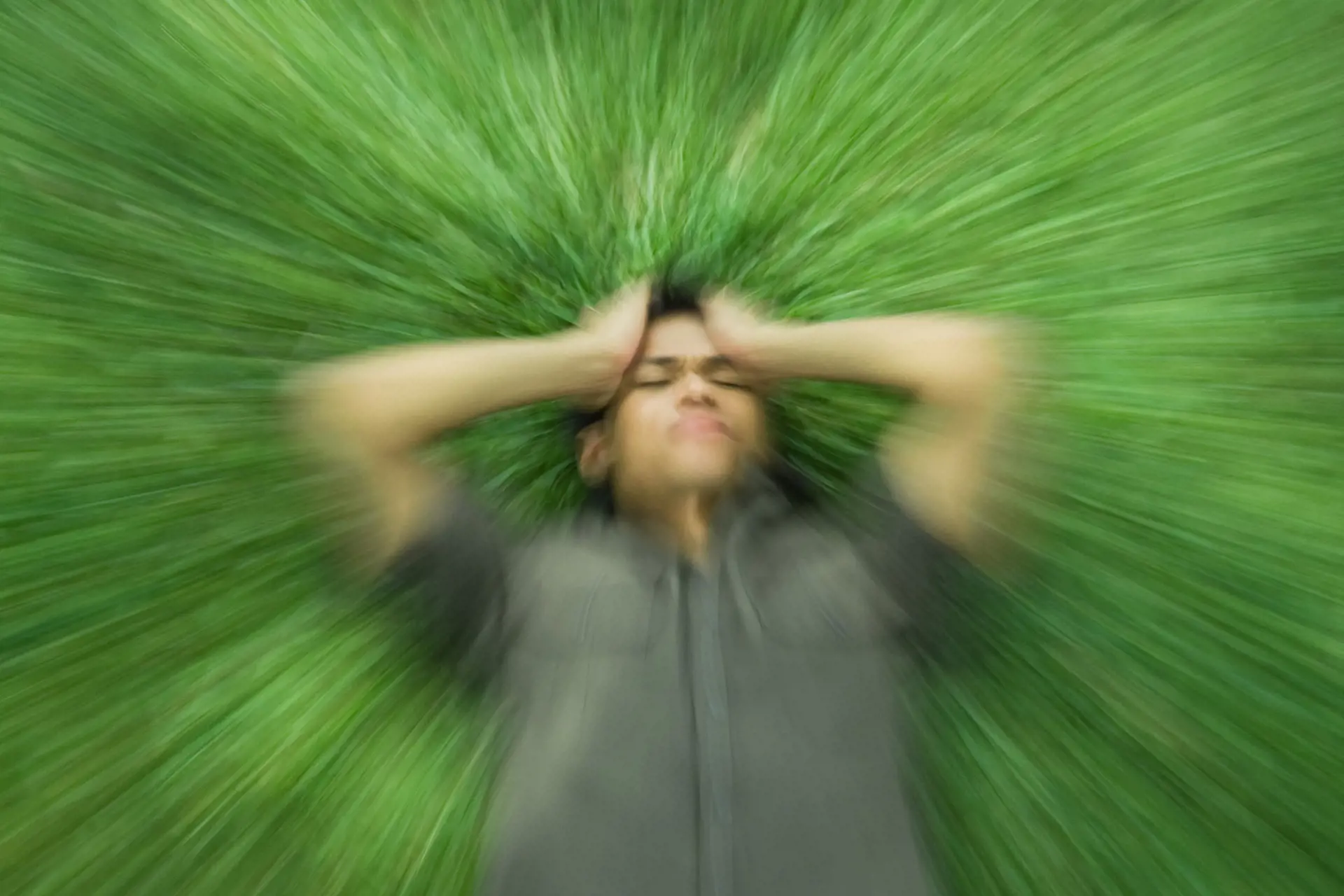 Bildet illustrerer en mann liggende i gresset med sterke smerter i hodet.
