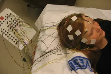 En jente som ligger på en seng, påkoblet masse ledninger til hodet,
