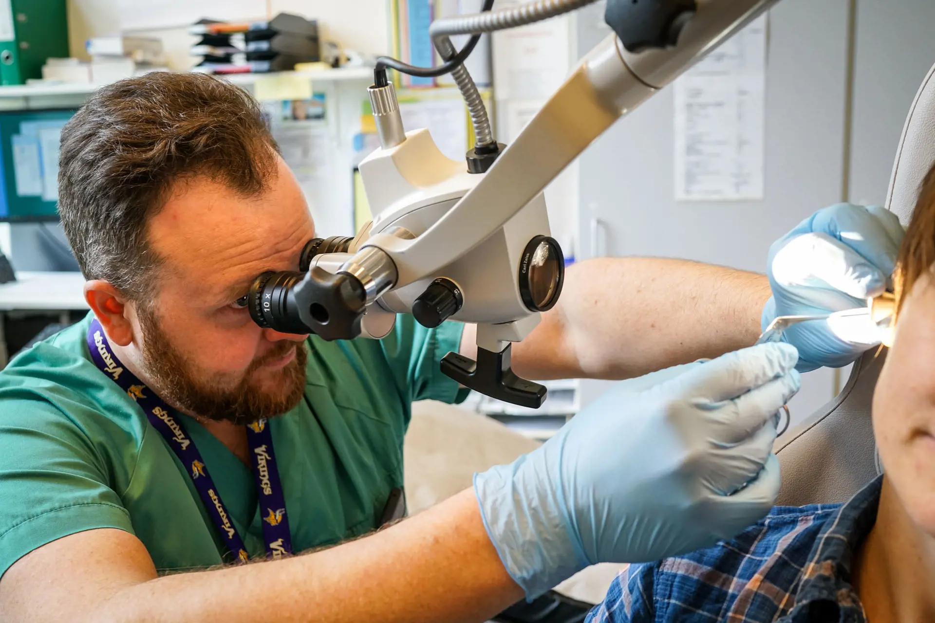 Lege som ser i et mikroskop inni øret til en pasient.
