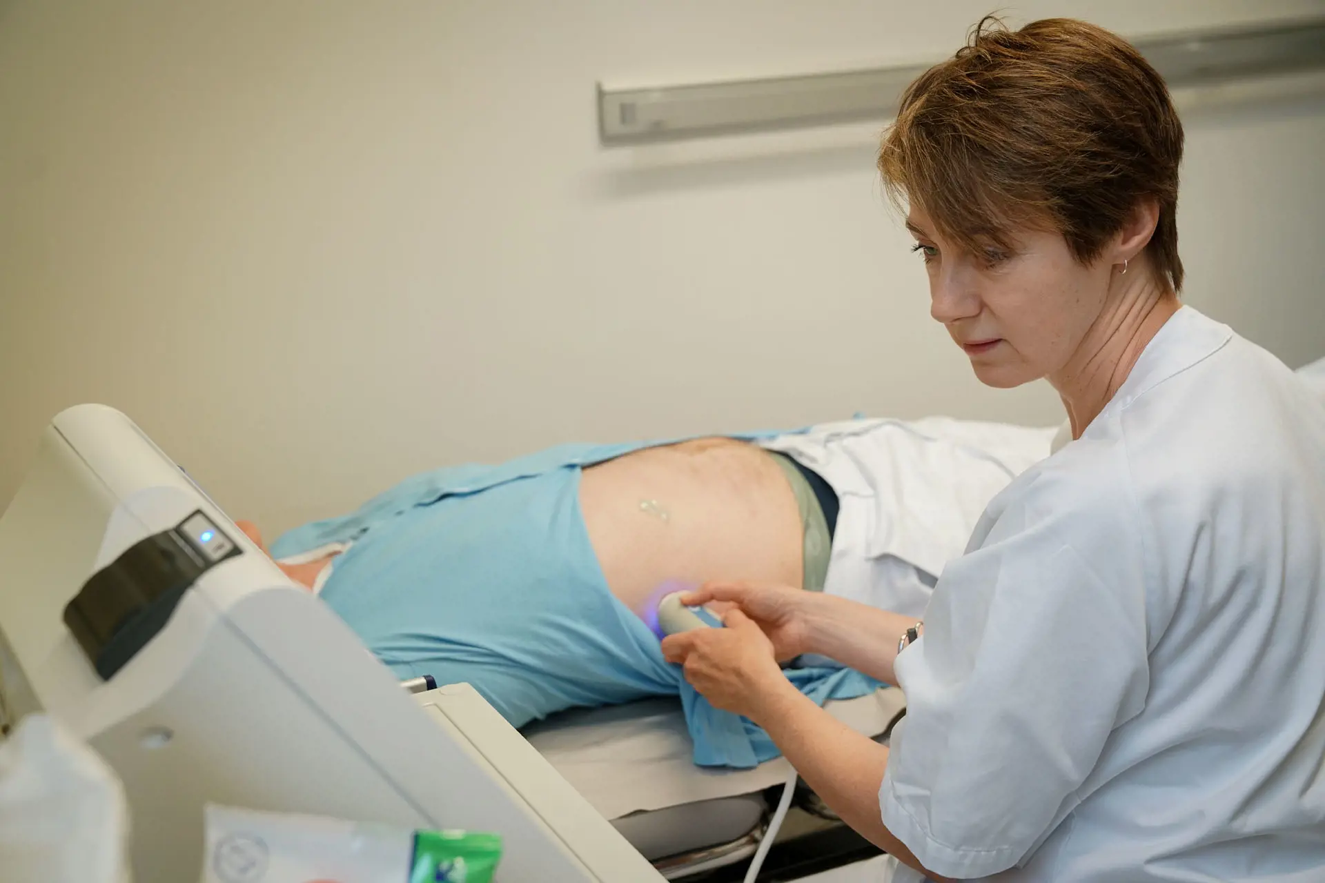 Kvinnelig lege gjør ultralyd av magen til en mannlig pasient.