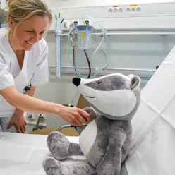 Bilde av en sykepleier i hvitt som hilser på en bamse-grevling.